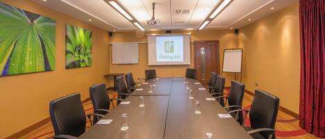A conference room with a long table, chairs, a projector screen, and a Holiday Inn banner.
