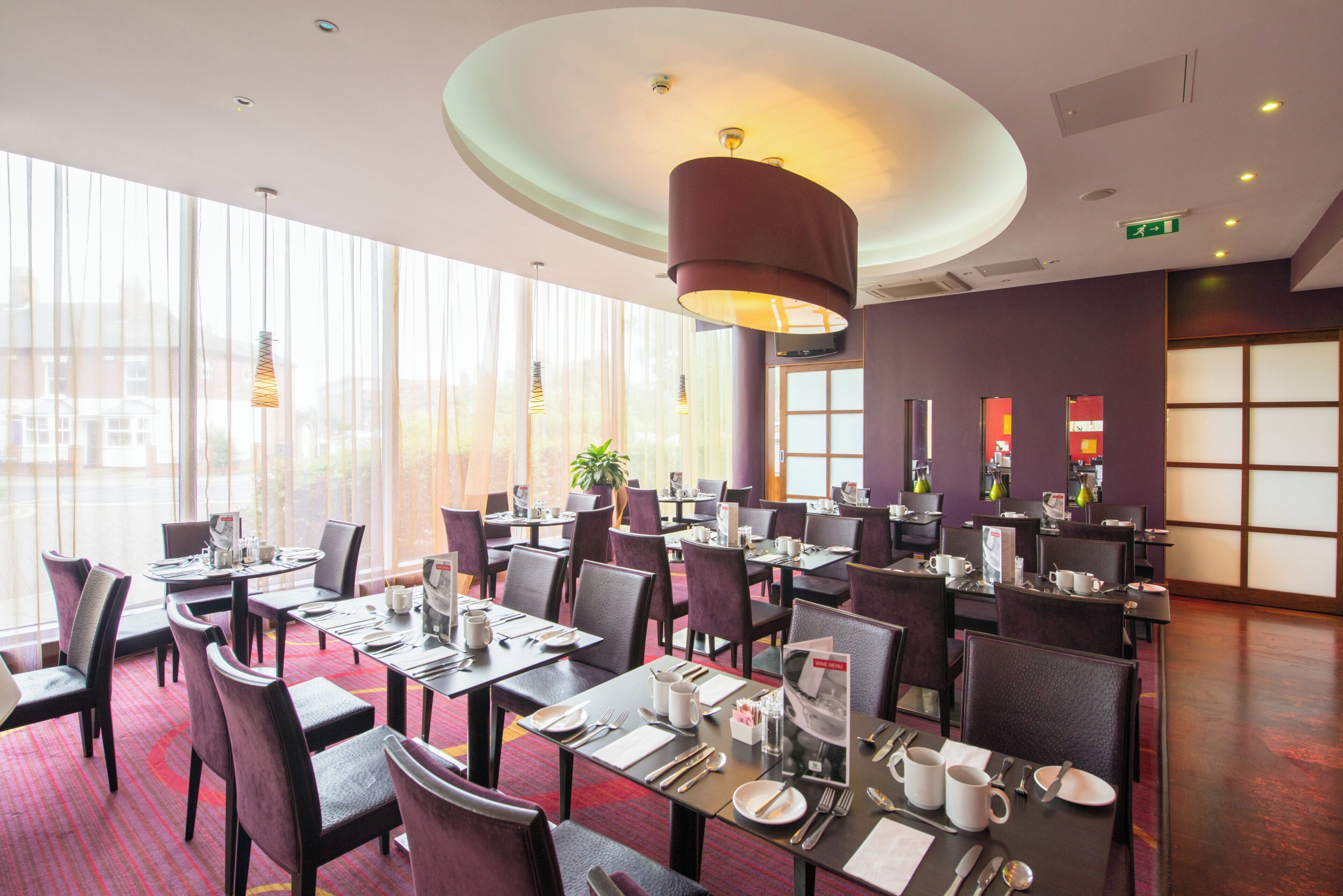 A restaurant with multiple tables and chairs, large windows, and a modern ceiling design.