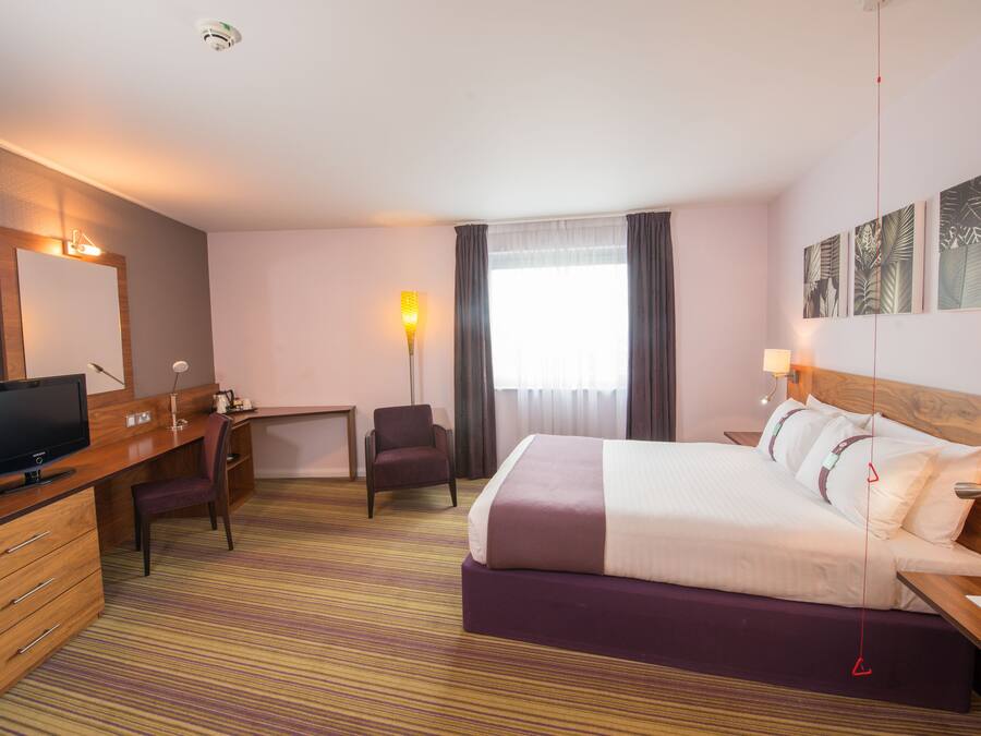 Een hotelkamer met een bed, bureau, stoel, televisie en kunst aan de muren.