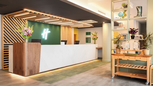 Un comptoir d’accueil moderne avec un revêtement en bois, un mur d’accent vert et une plante décorative.