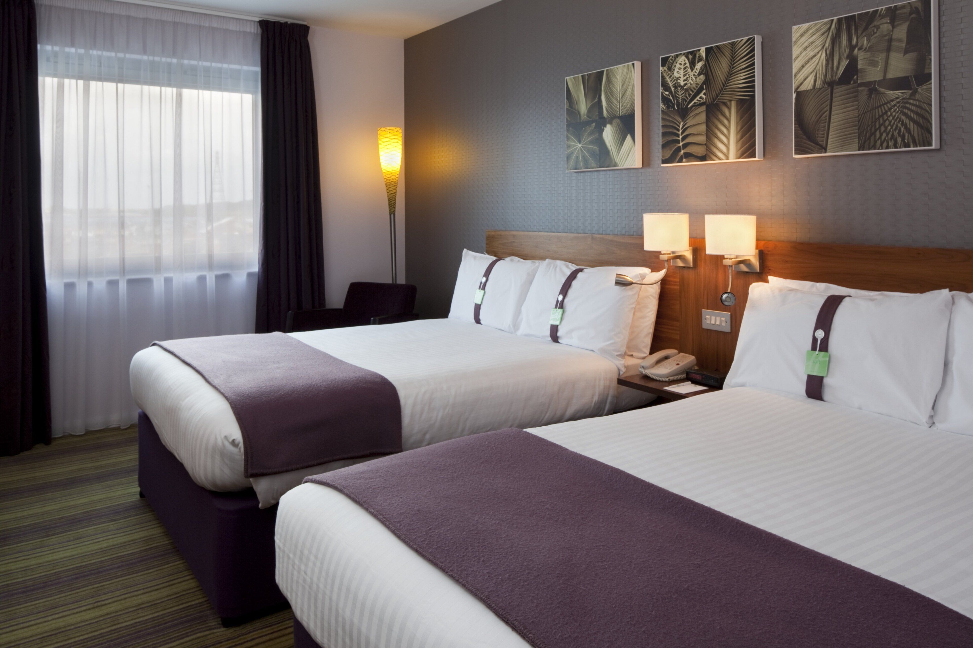 A hotel room with two beds, a desk, a phone, and a lamp.