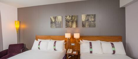 A hotel room with two beds, a nightstand with a phone, and a lamp.