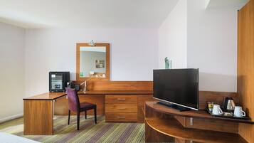 Ett hotellrum med ett skrivbord i trä, en tv, en stol, en säng och en randig matta.