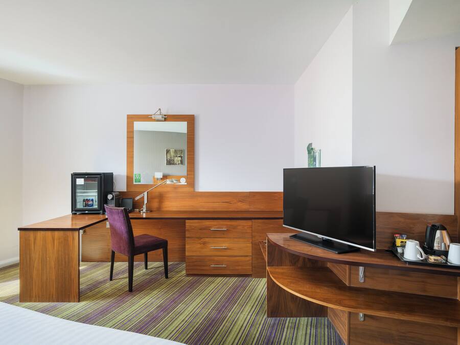 Ett hotellrum med ett skrivbord i trä, en tv, en stol, en säng och en randig matta.