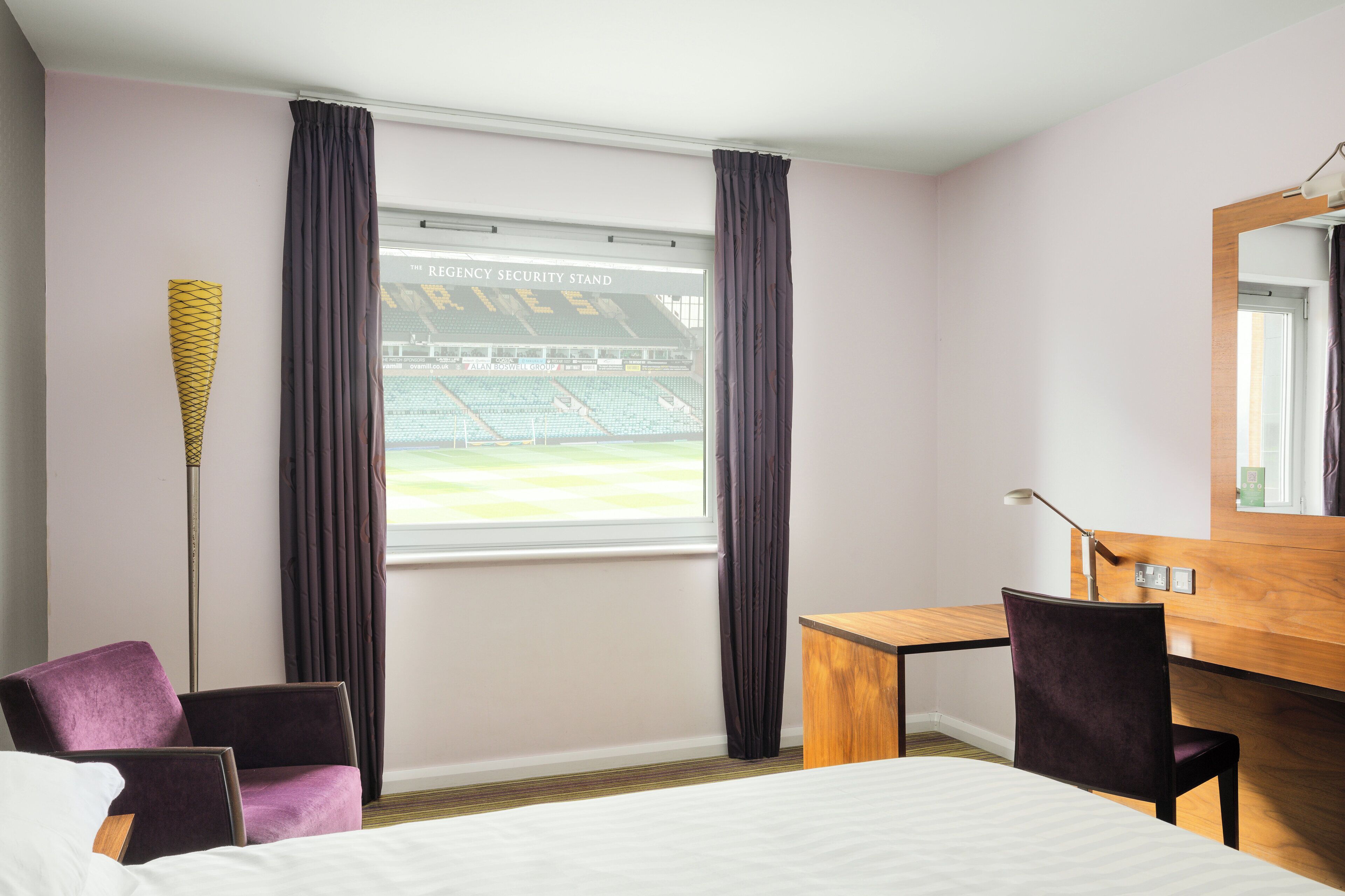 A hotel room with a bed, a desk, a chair, a lamp, and a window with curtains.