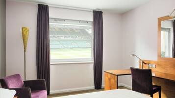 A hotel room with a bed, a desk, a chair, a lamp, and a window with curtains.