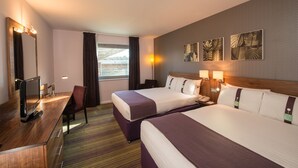 Une chambre d’hôtel avec deux lits, un bureau avec un ordinateur, une chaise et des œuvres d’art accrochées au mur.