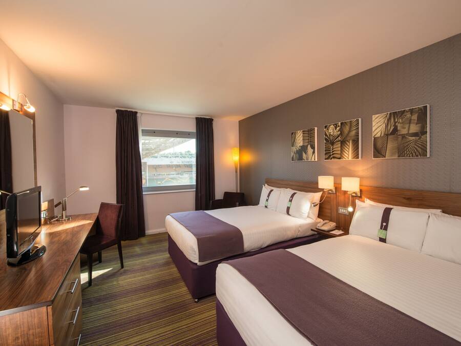 A hotel room with two beds, a desk with a computer, a chair, and artwork on the wall.