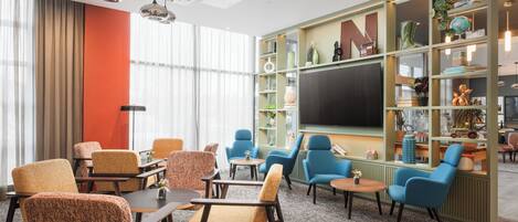 A modern lounge area with comfortable seating, a large bookshelf, and a flat-screen TV.