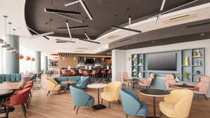 A modern lounge area with seating, a bar, and a large TV screen. - Holiday Inn Norwich City by IHG (Norwich)