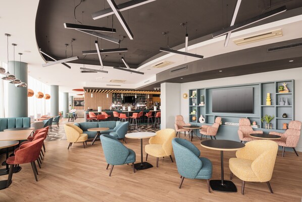 A modern lounge area with seating, a bar, and a large TV screen. - Holiday Inn Norwich City by IHG (Norwich)