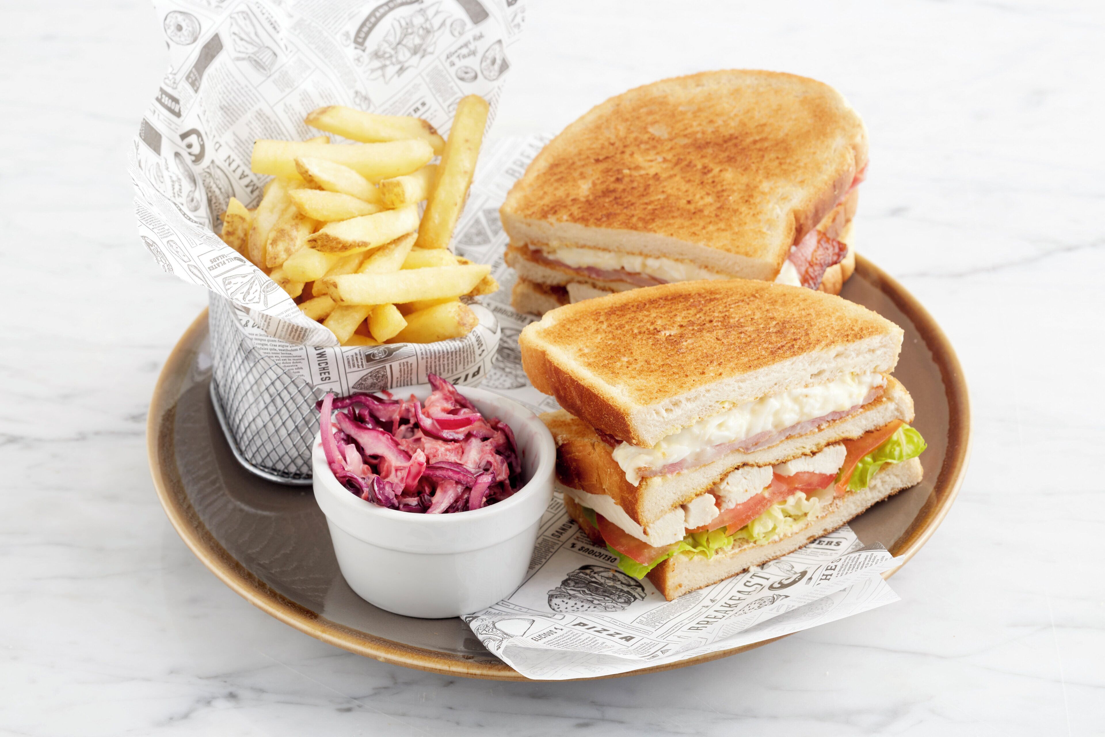 Een bord met een sandwich, frietjes en een salade van witte kool.