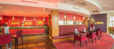 A modern restaurant interior with a curved layout, red seating, a bar area, and pendant lighting.