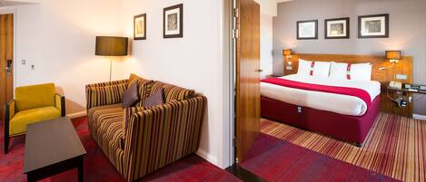 A hotel room with a bed, a sofa, a chair, and a small table.