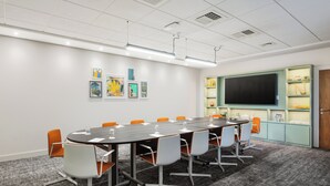 A conference room with a long table, white and orange chairs, a projector screen, and a display cabinet with various items. - Holiday Inn Norwich City by IHG (Norwich)
