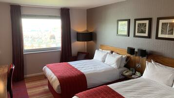 A hotel room with two beds, a desk, a chair, a lamp, and a window with curtains.