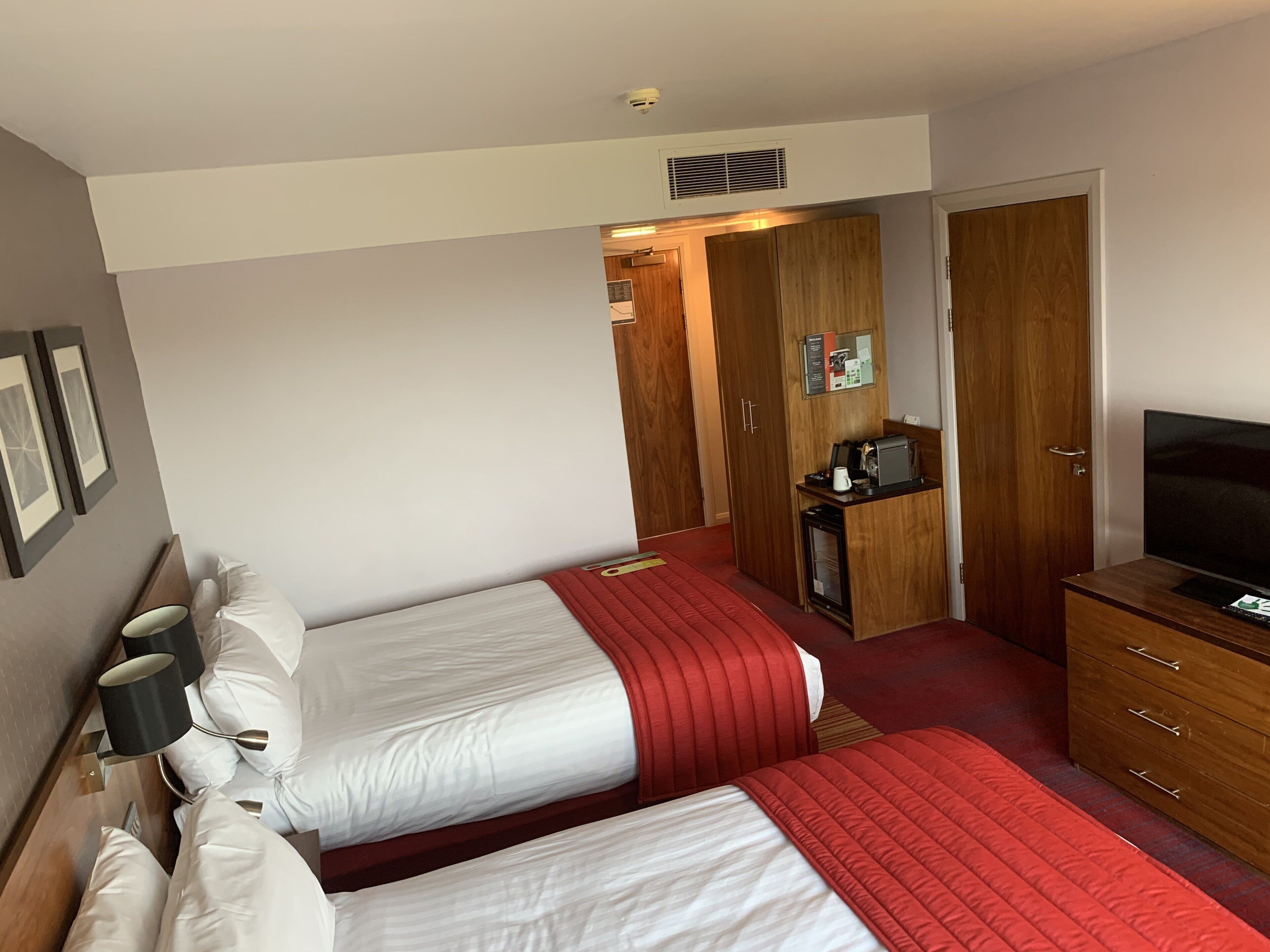 Hotellihuone, jossa on kaksi sänkyä, televisio, minibaari ja puinen vaatekaappi.