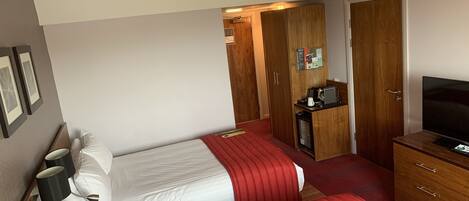 Ein Hotelzimmer mit zwei Betten, einem Fernseher, einer Minibar und einem Holzschrank.