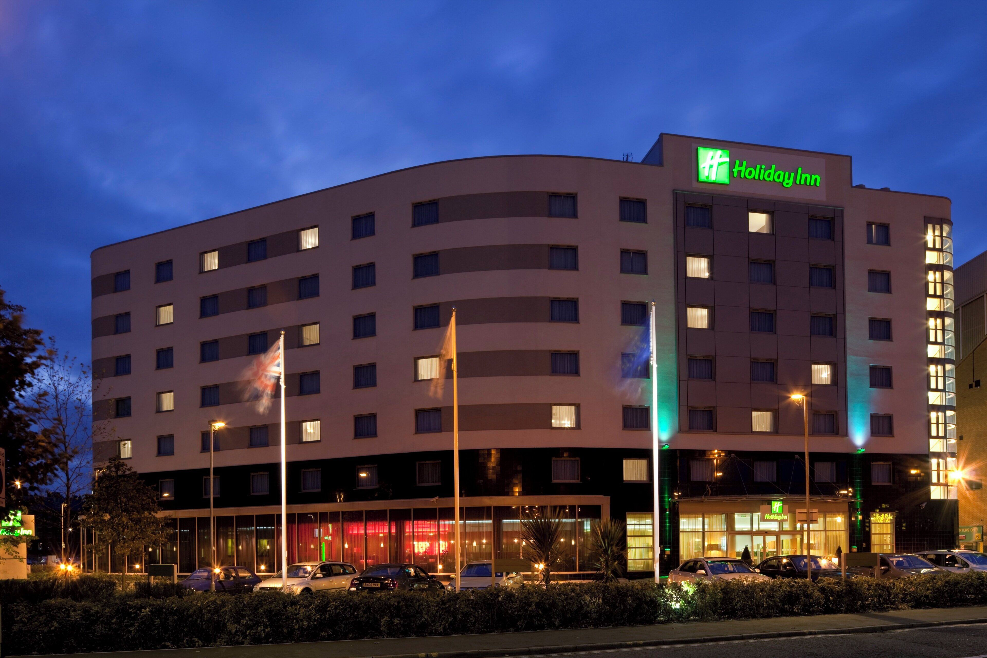 Un hotel Holiday Inn con varios pisos, fachada plana y un estacionamiento con coches.