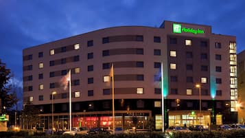 Un hotel Holiday Inn con varios pisos, fachada plana y un estacionamiento con coches.