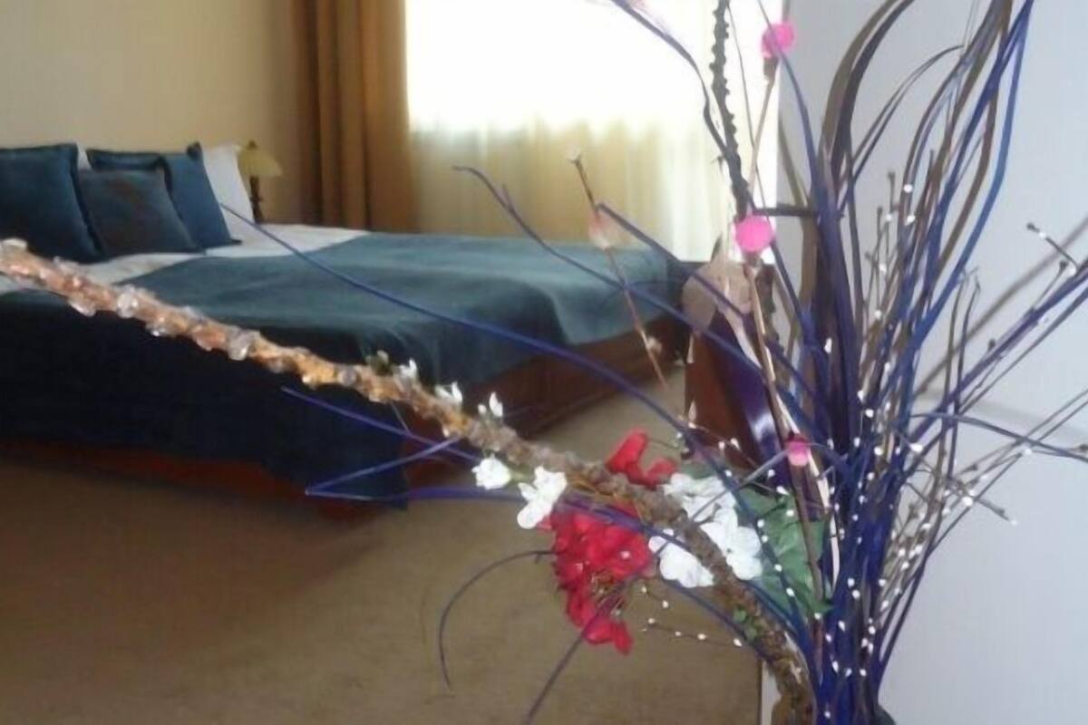 Quarto de hotel com cama, mesa de cabeceira e um ramo decorativo com flores.