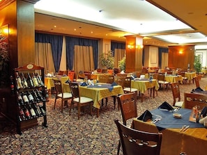 A hotel dining area with multiple tables and chairs, a wine rack, and curtains on the windows. - Emerald Spa Hotel (Bansko)