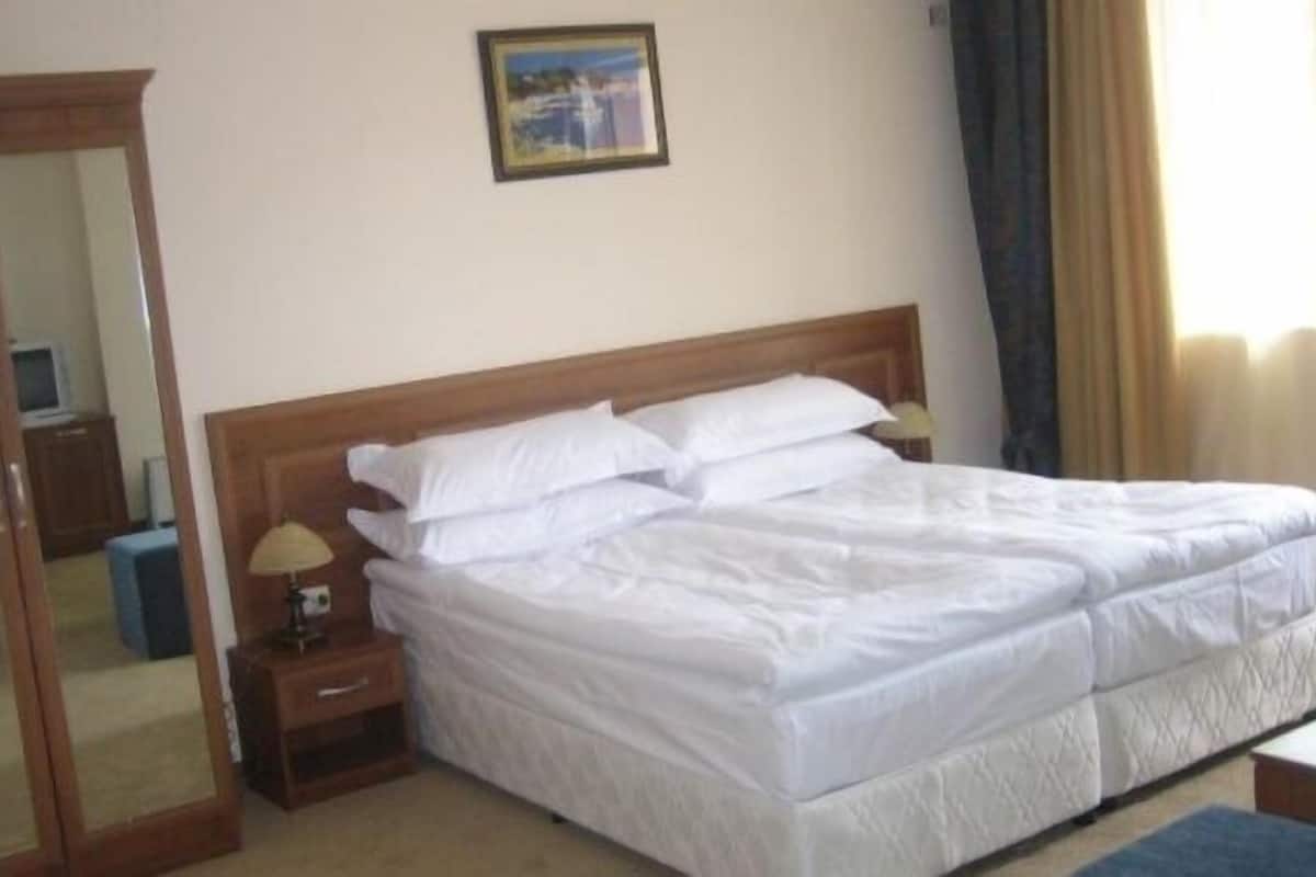 Quarto de hotel com uma cama grande, uma mesa de cabeceira com abajur, um pequeno armário, um espelho e um quadro na parede.
