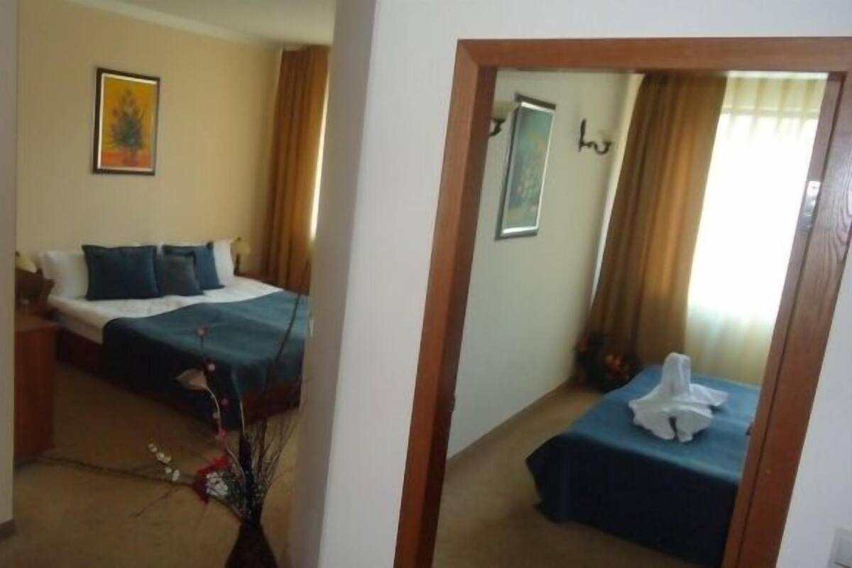 Quarto de hotel com cama, mesa de cabeceira, escrivaninha, cadeira, mesinha e espelho.