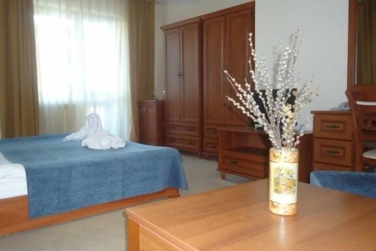 Quarto de hotel com uma cama, uma cômoda de madeira e um vaso com flores.