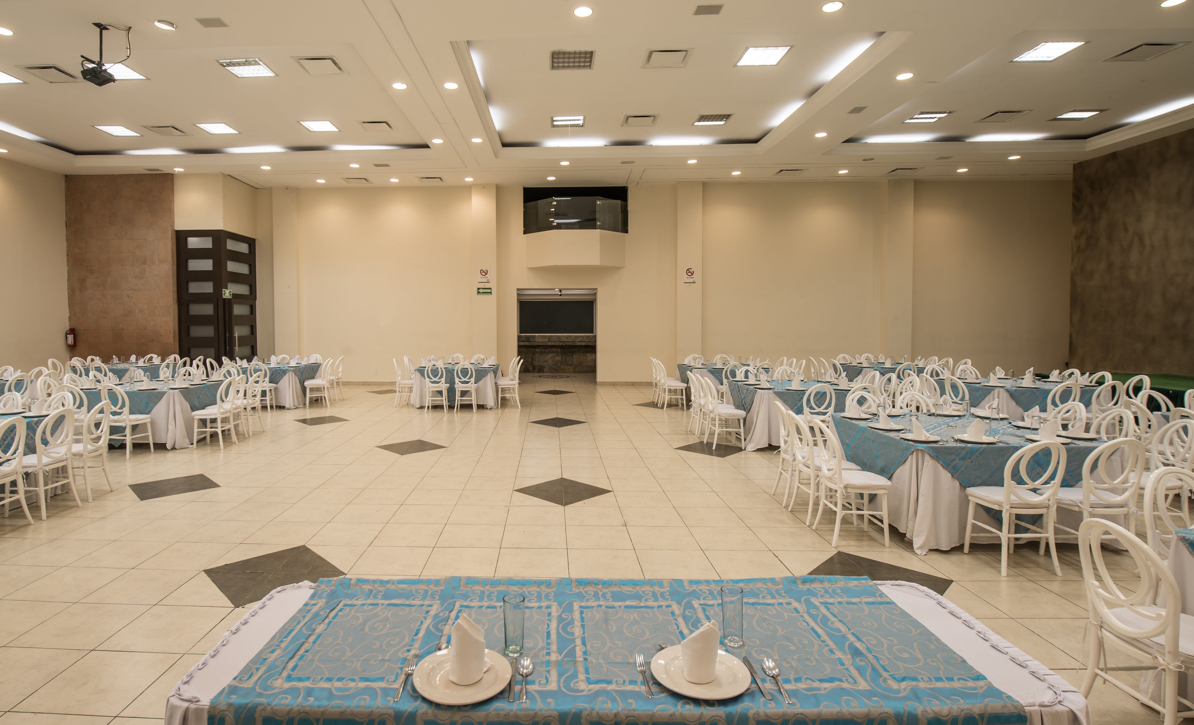 Une grande salle de conférence équipée de plusieurs tables et chaises, d’un projecteur et d’un écran au plafond.