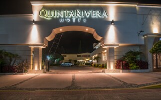 A entrada do Hotel Quintarivera, com uma placa de destaque, um caminho de entrada pavimentado e paisagismo ao redor.
