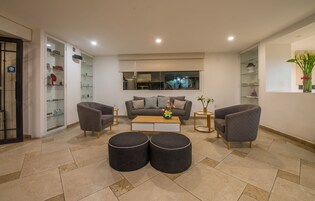 Uma sala de estar moderna com um sofá cinzento, duas poltronas, uma mesa de centro e um aparador de vidro com objetos decorativos.