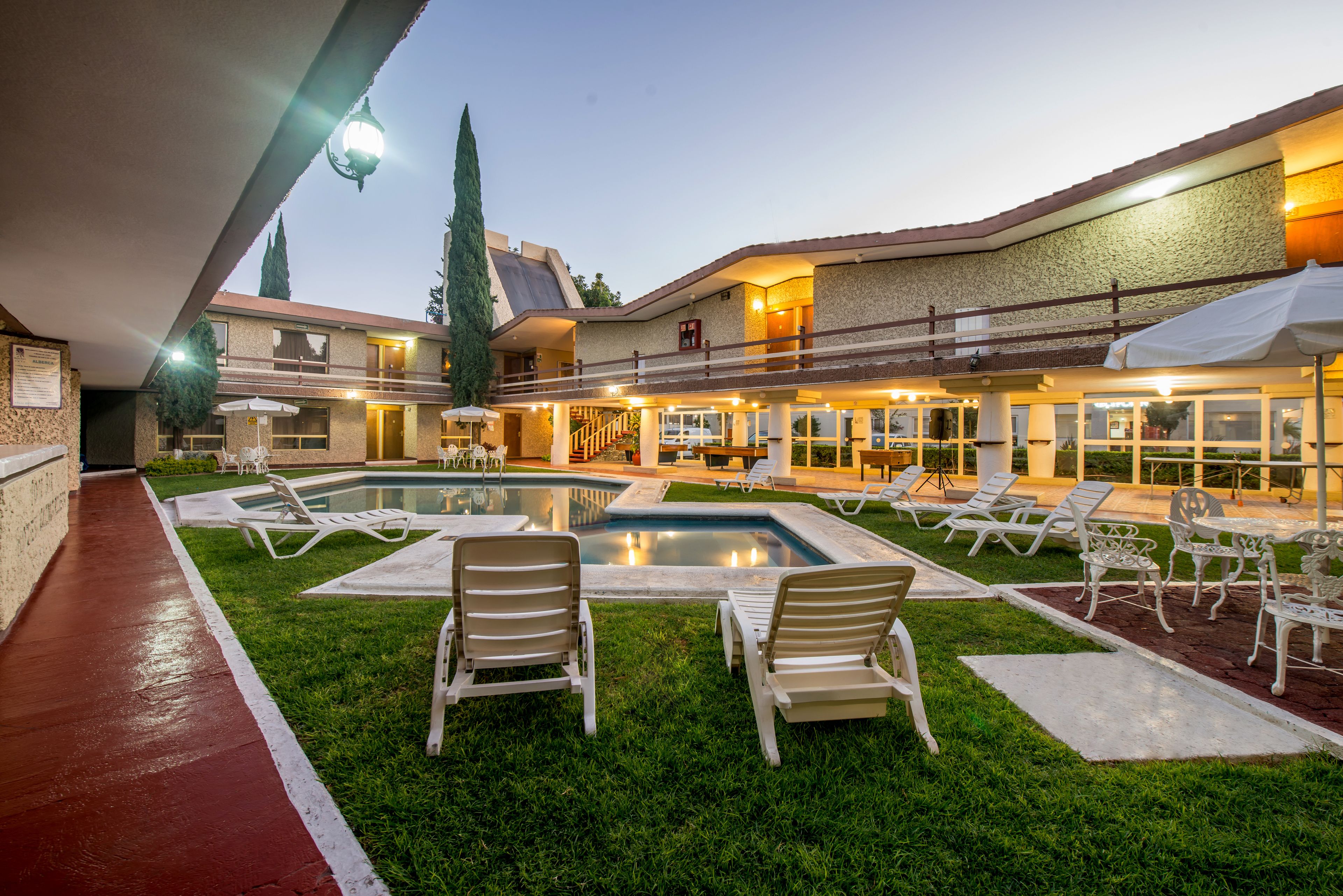 Un patio de hotel con piscina, sillones de descanso y una zona de estar cubierta.