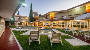 Un patio de hotel con piscina, sillones de descanso y una zona de estar cubierta.