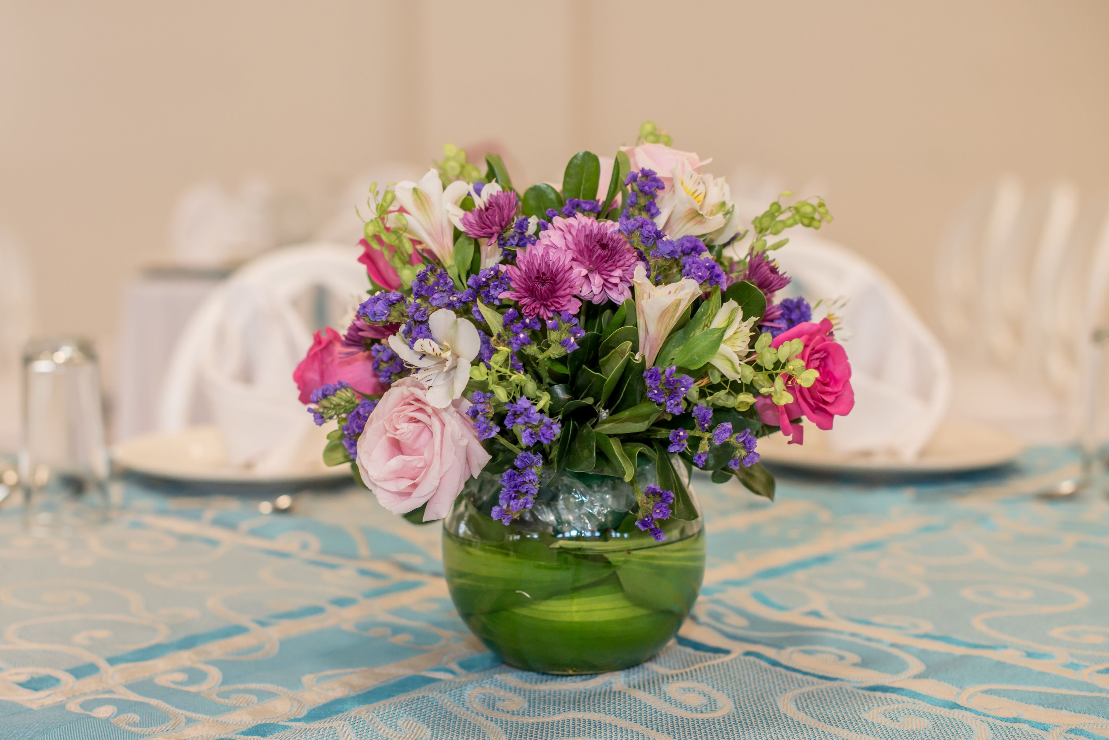 En grøn vase med blomsterarrangement på et bord med blåternet dug.