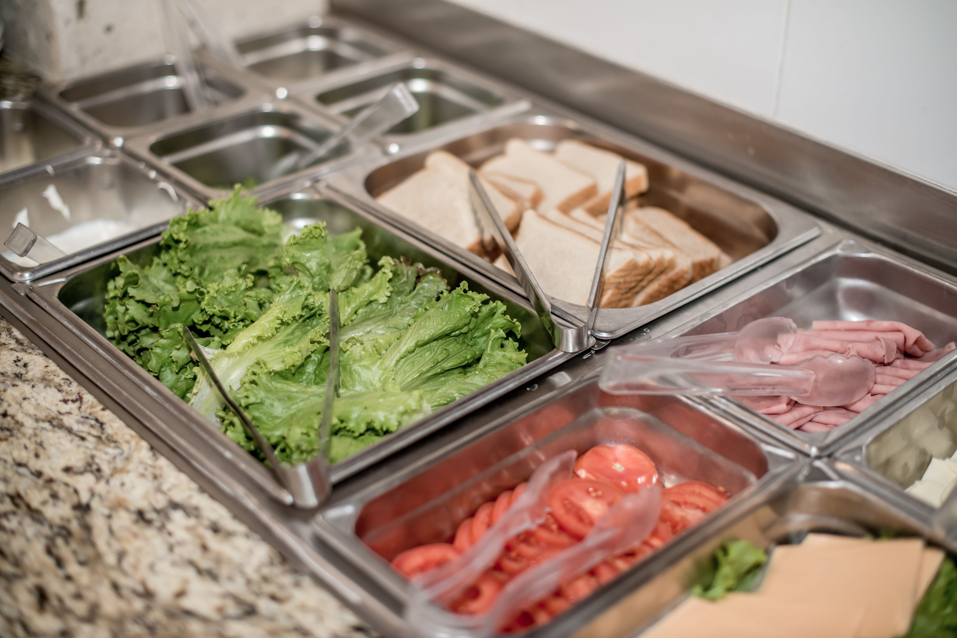 A buffet with various food options including lettuce, sliced tomatoes, and sliced bread.
