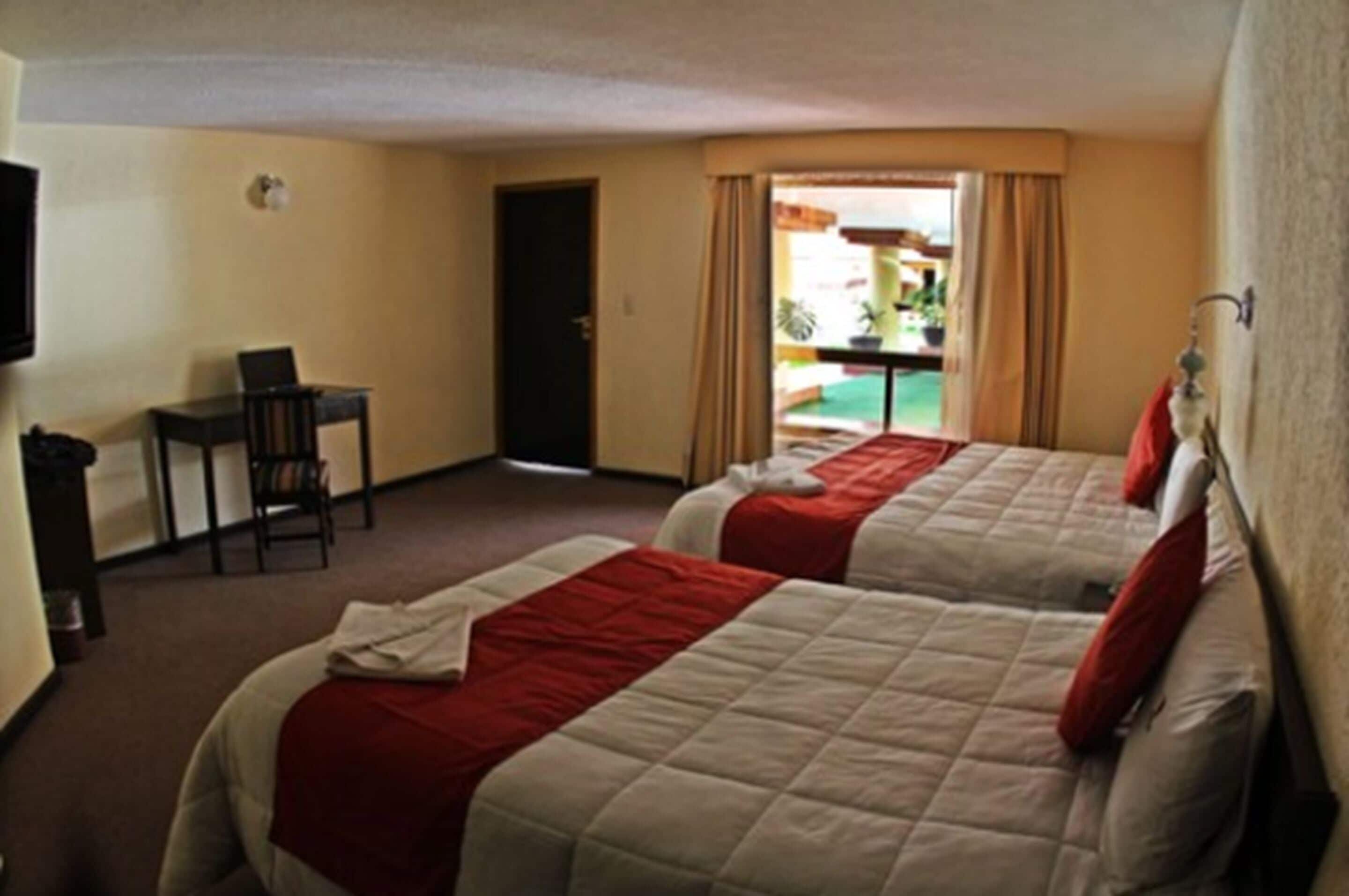 A hotel room with two beds, a desk, and a chair.