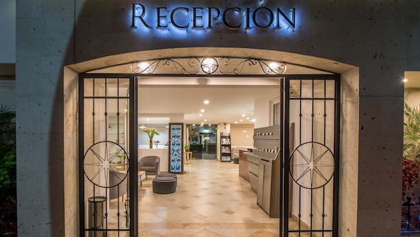 Uma área de recepção com piso de azulejos, balcão de atendimento e uma grande placa decorativa sobre a entrada.
