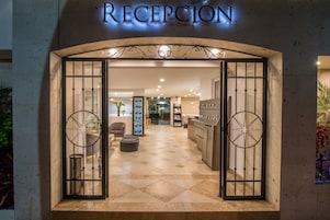 Uma área de recepção com piso de azulejos, balcão de atendimento e uma grande placa decorativa sobre a entrada.