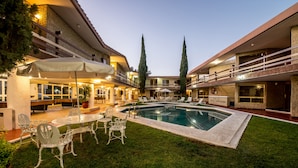 Pátio de hotel com piscina, área de estar ao ar livre e gramado bem cuidado.