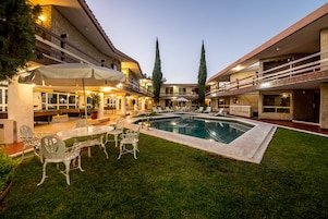 Pátio de hotel com piscina, área de estar ao ar livre e gramado bem cuidado.
