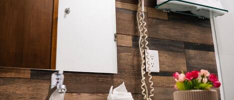 Un baño con pared de madera, un perchero blanco, un secador de pelo y un florero con flores.