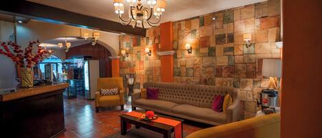 Un vestíbulo de hotel con sofá, sillas, una mesa de centro, una araña y una pared de piedra.