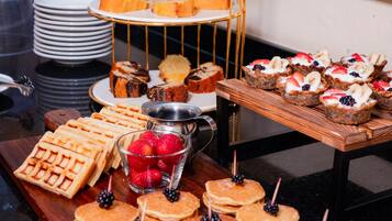 A buffet table with various desserts and pastries, including waffles, pancakes, and a tiered cake stand with assorted baked goods.