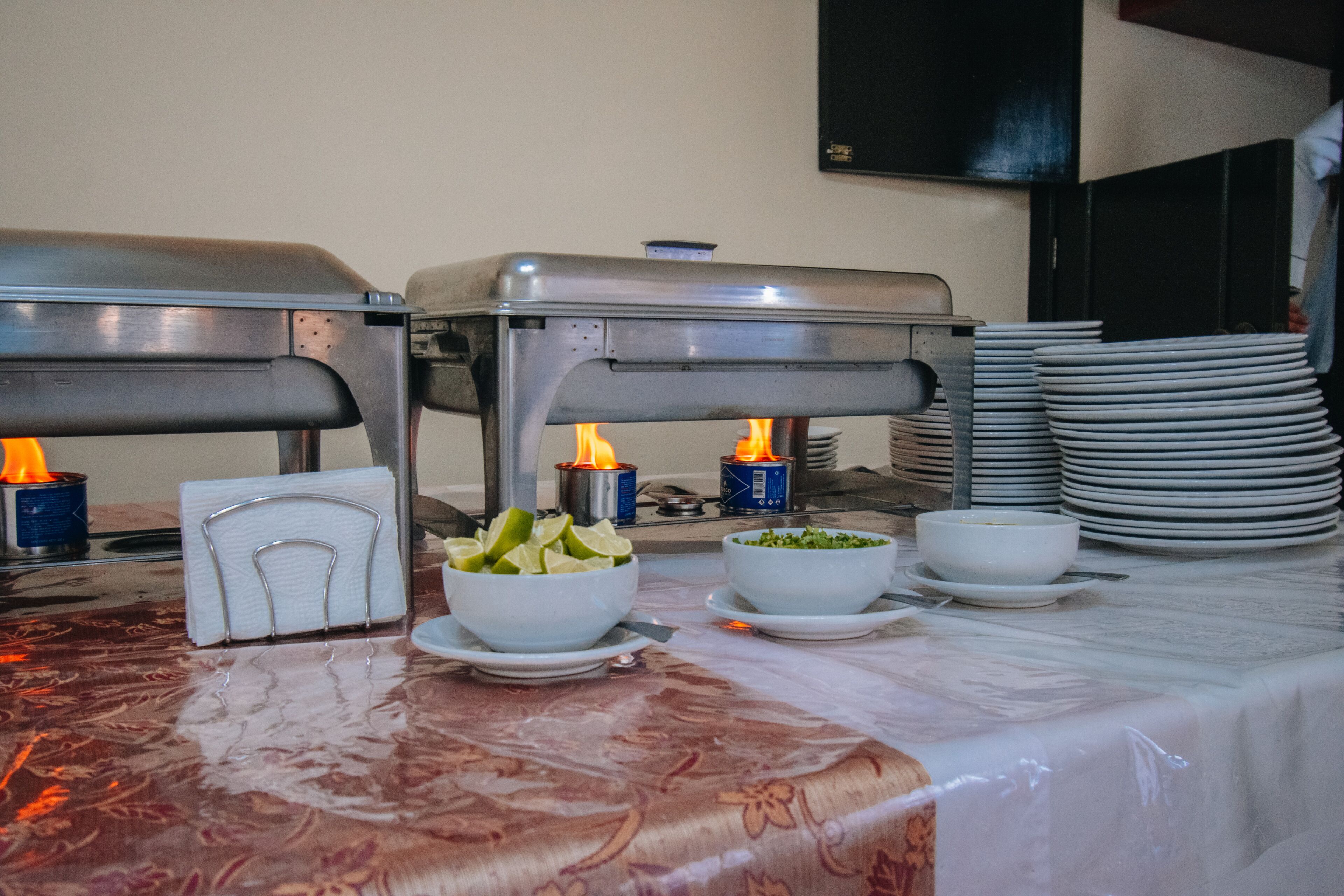 A buffet setup with food stations, napkins, and stacked plates.