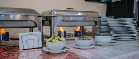 A buffet setup with food stations, napkins, and stacked plates.