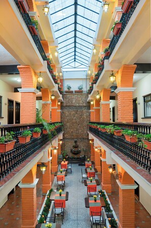Ein mehrgeschossiges Atrium mit einer zentralen Fontäne, Balkonen mit Topfpflanzen und Sitzbereichen im Freien.
