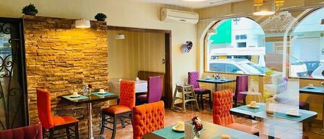 A restaurant with a stone wall, orange and purple upholstered chairs, and tables with placemats.