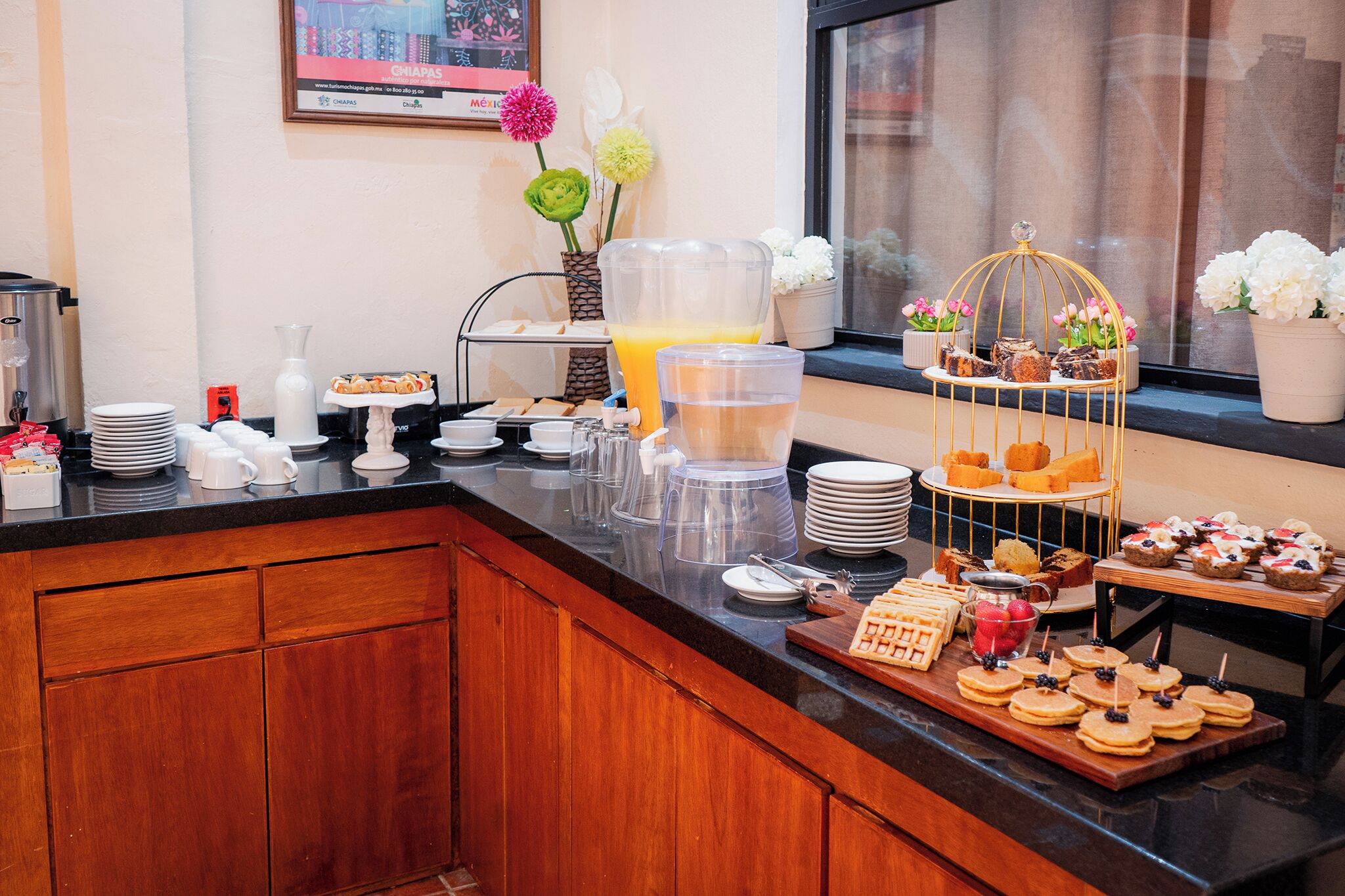 Una mesa de buffet con diversas opciones de comida, un dispensador de ponche de frutas y flores decorativas.