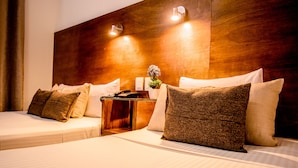 Une chambre d’hôtel avec deux lits, une tête de lit en bois, des lampes de chevet, une table de chevet et un vase avec des fleurs.